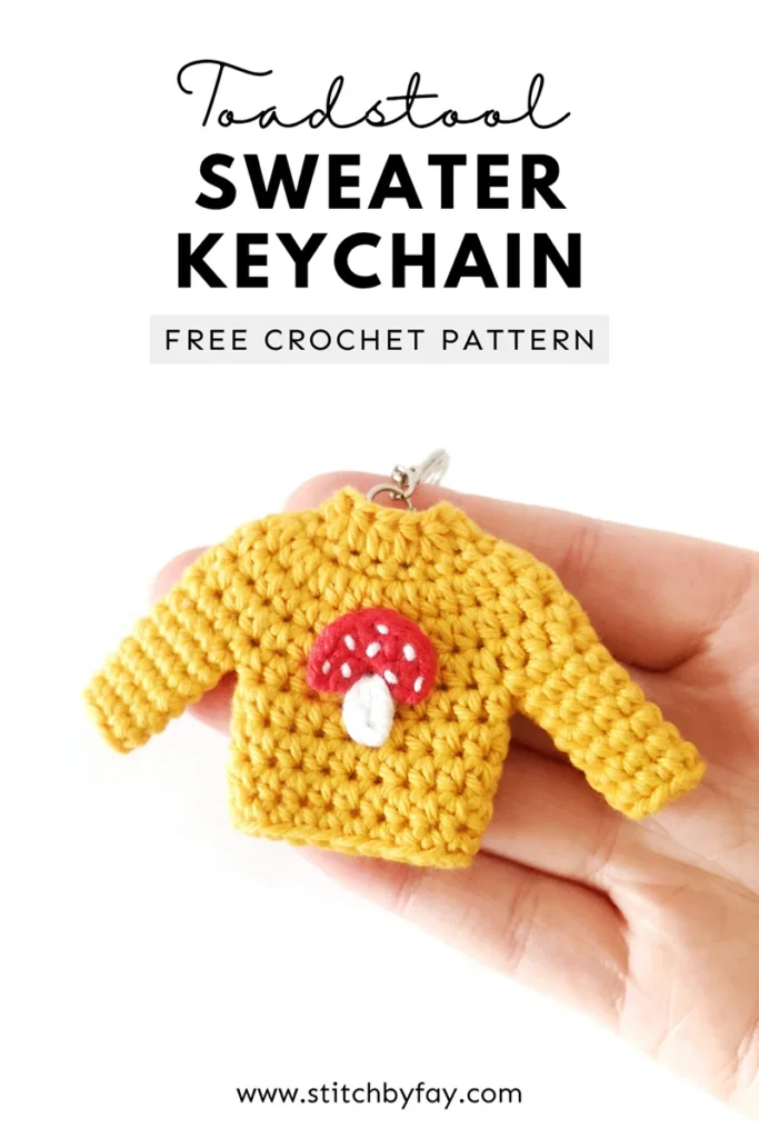 Pinterest image showing a yellow mini crochet sweater keychain with a red and white applique on the front, being held up by a hand. Text overlay reads: "Toadstool sweater keychain, free crochet pattern, www.stitchbyfay.com".