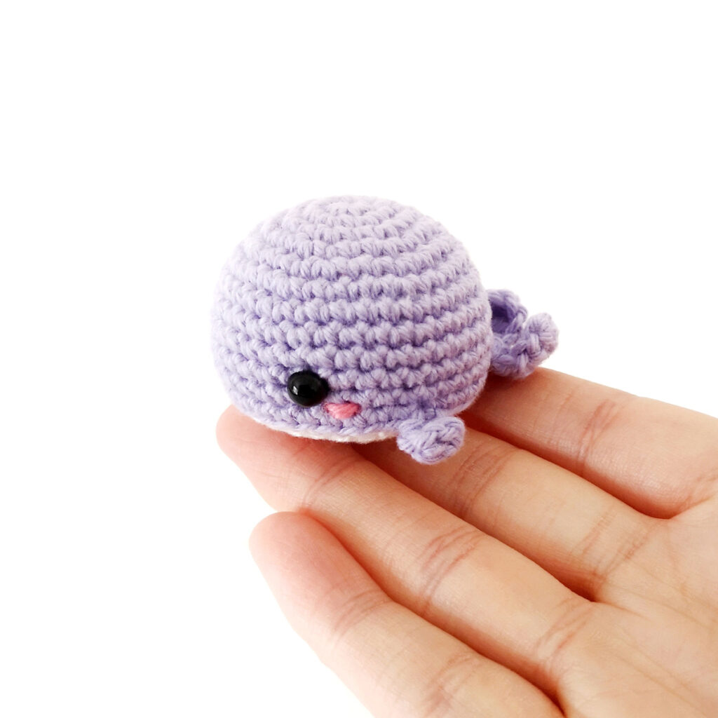 Crochet whale sitting on the end of a hand.