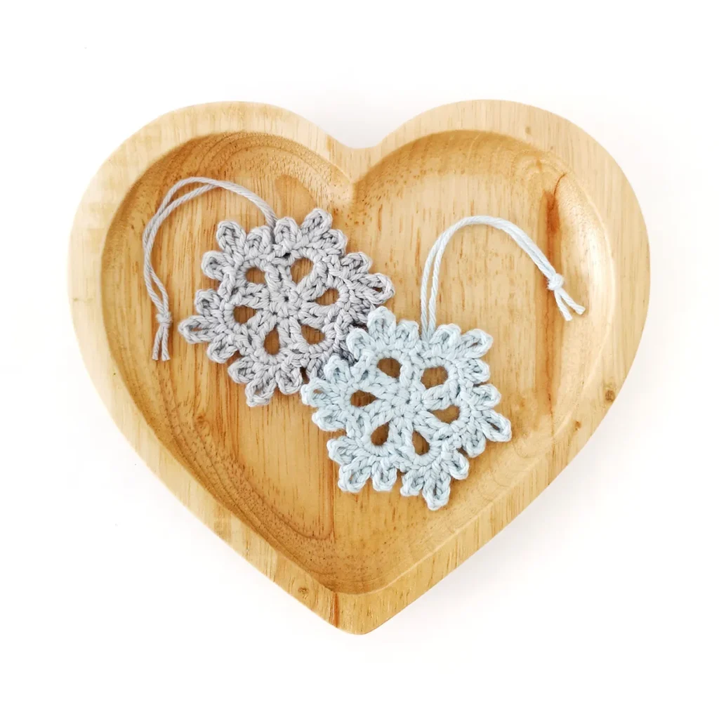 Two crochet snowflakes lying side by side on a small heart shaped tray.