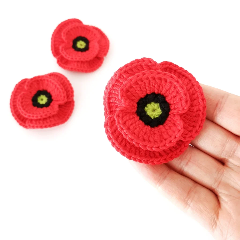 A red crochet poppy being held up with 2 red crochet poppies in the background.