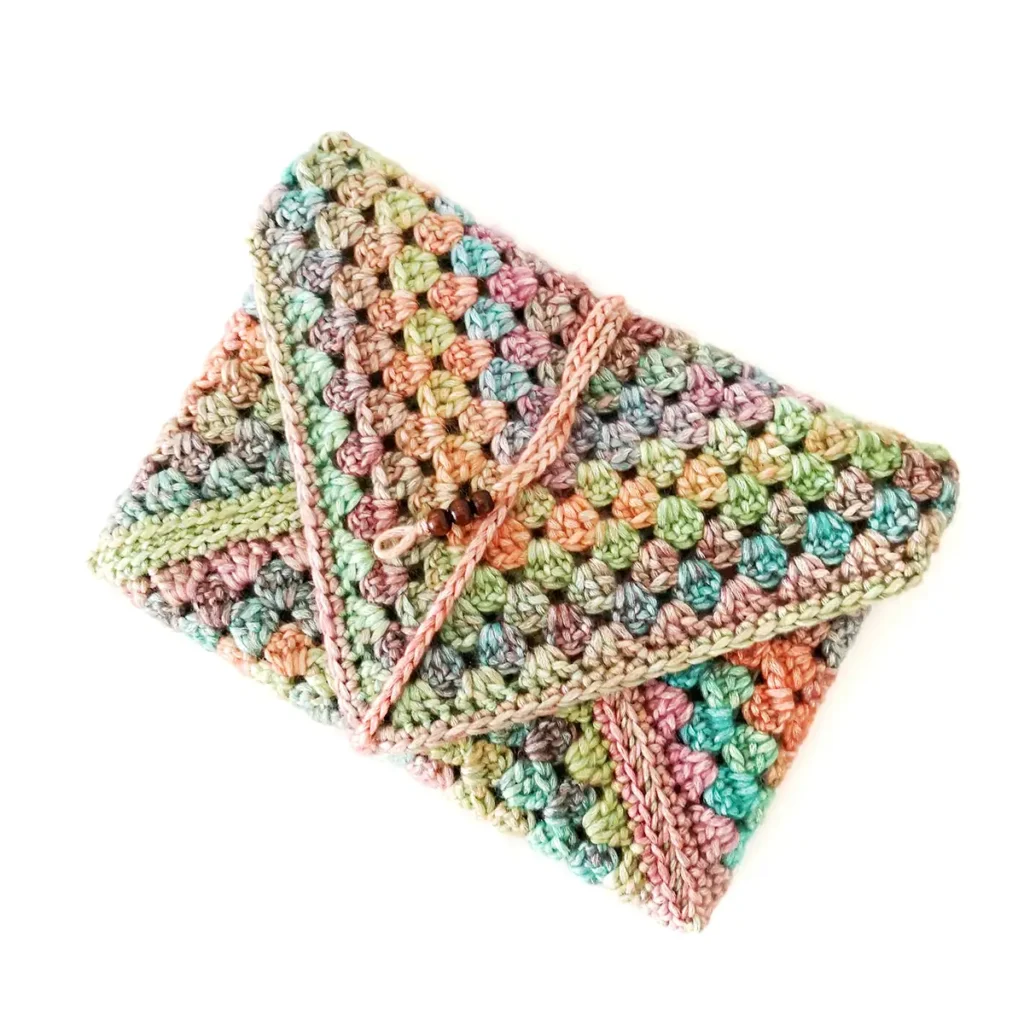 A closed multicoloured crochet book sleeve with a beaded tie on a white background.