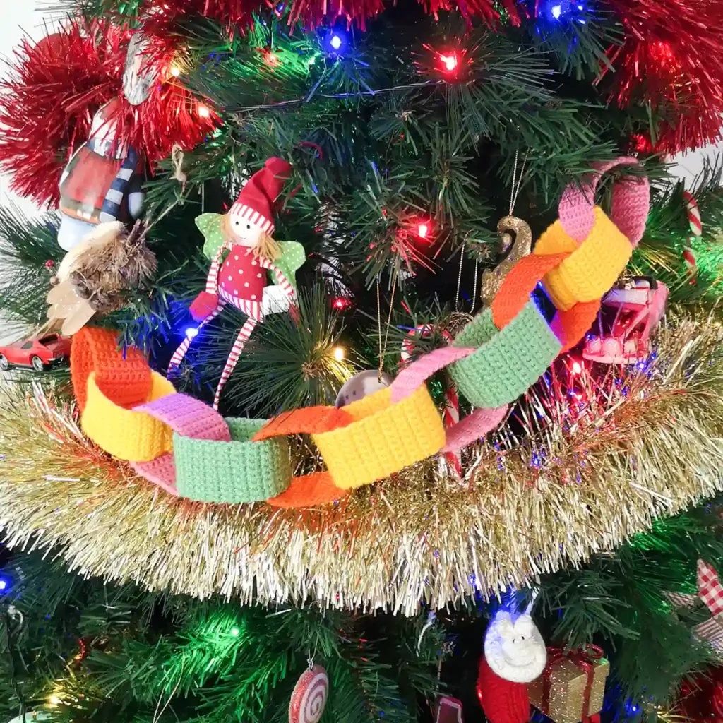 Short crochet paper chain garland with orange, yellow, pink and green chain links displayed on a Christmas tree.