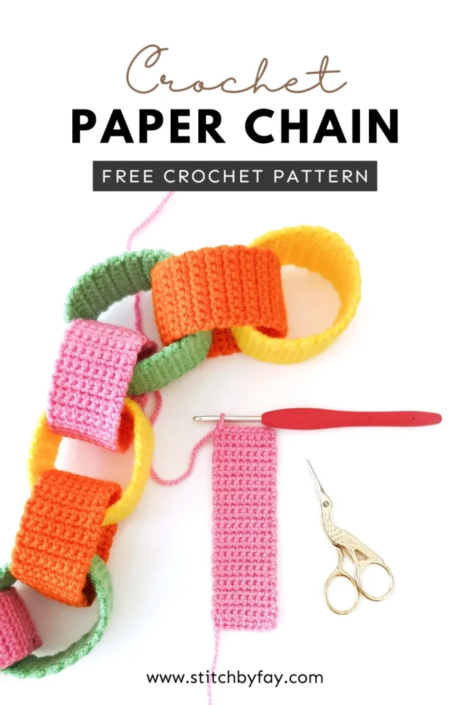 Pinterest image showing a crochet paper chain garland with orange, yellow, pink and green chain links, next to an in progress pink crochet strip with a crochet hook and a pair of gold scissors. Text overlay reads: "Crochet paper chain, free crochet pattern, www.stitchbyfay.com".