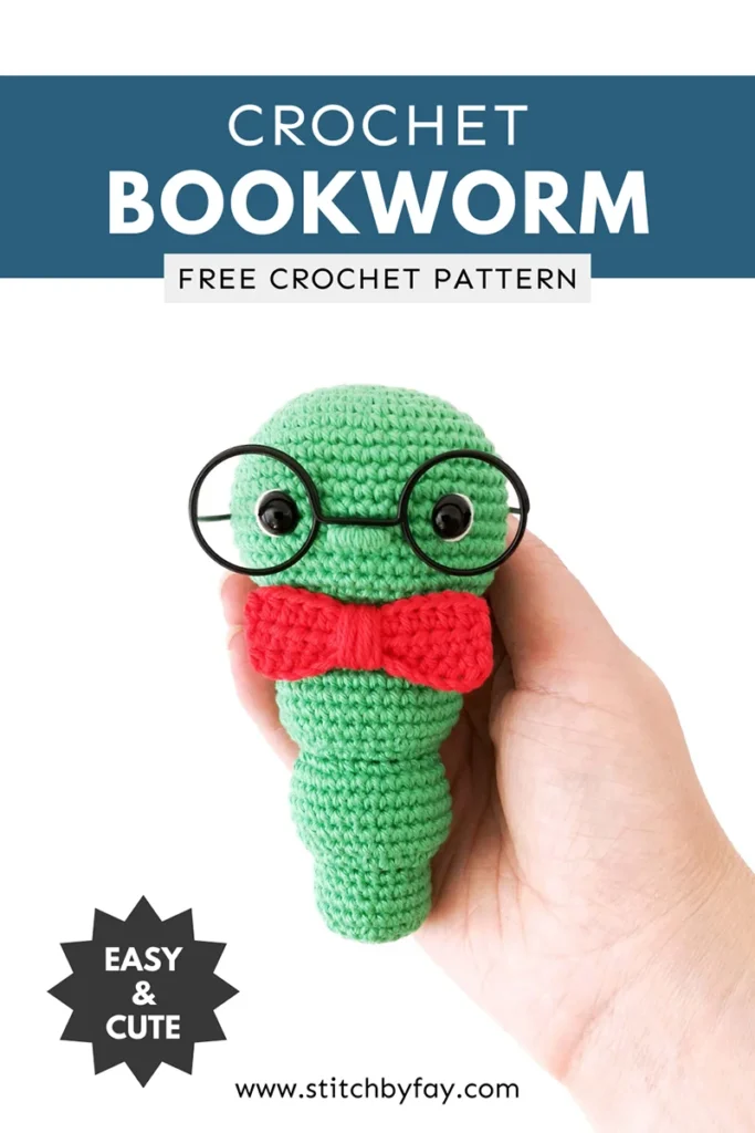 Pinterest image showing a green crochet bookworm with red bow tie and oversized black rimmed glasses being held in a hand against a white background. Text overlay reads: "Crochet bookworm, free crochet pattern, www.stitchbyfay.com" with "easy & cute" in a starburst.