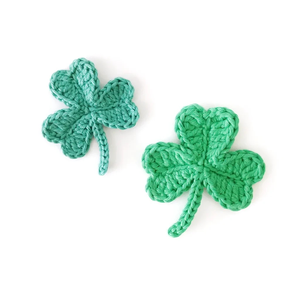 Two green crocheted shamrocks next to each other against a white background.