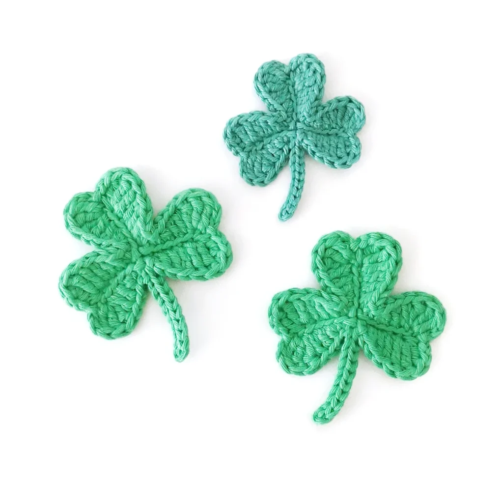 Three green crocheted shamrocks arranged together on a white background.