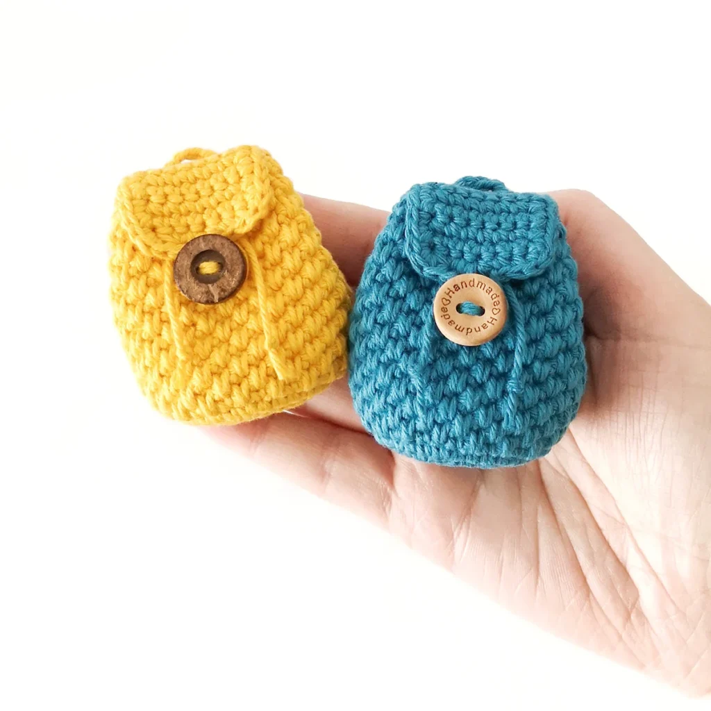 Two crochet mini backpack coin pouches, one blue and one yellow, lying on a hand.