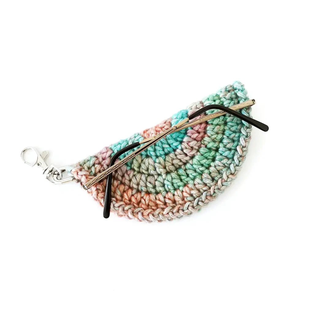 The back of a multicoloured crochet glasses case with silver lobster clasp and the arms of the glasses folded over the back.
