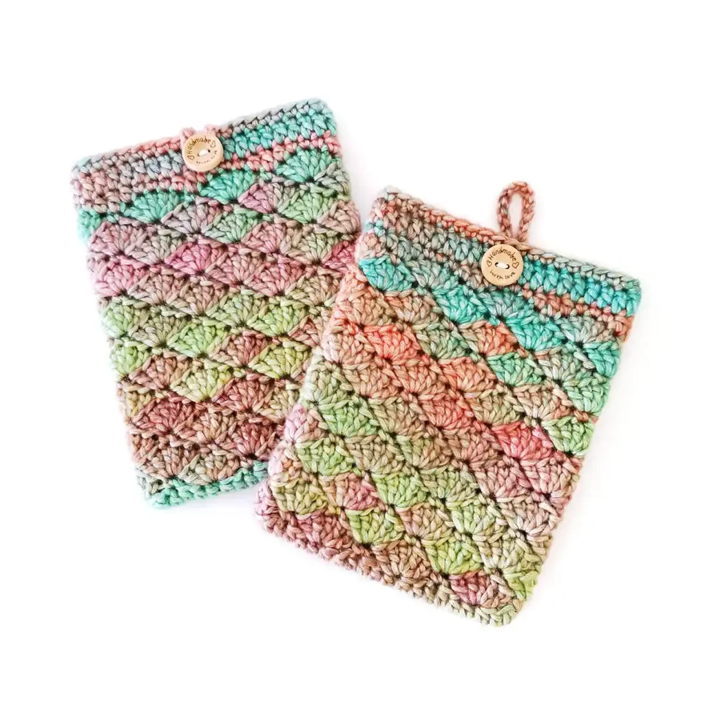 Two crochet kindle covers lying overlapping slightly, featuring the shell stitch and made with soft gradient yarn in shades of green, blue, orange and purple, with a round wooden button and loop closure.