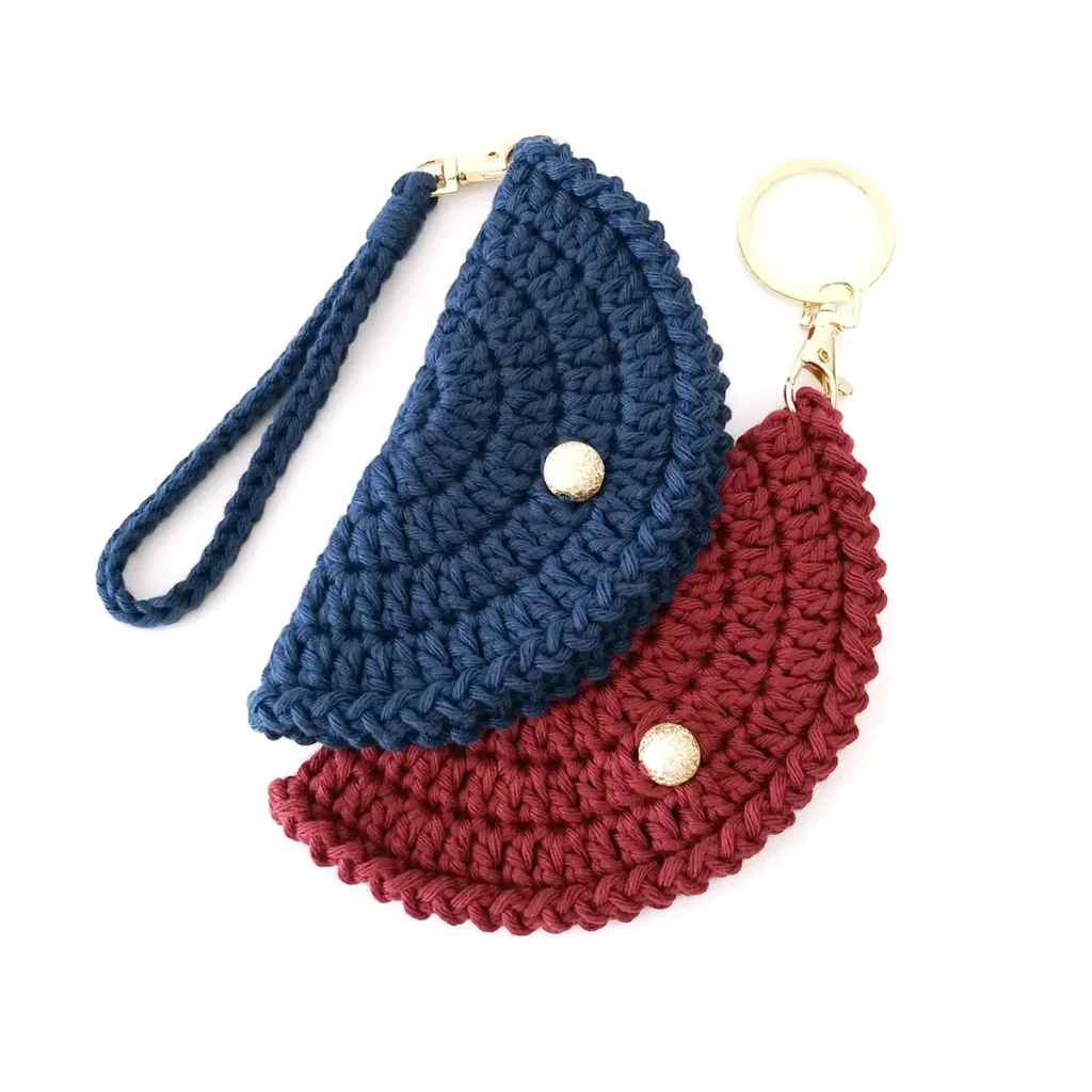 Two crochet glasses cases slightly overlapping, one red and one blue with gold keychain clasps and round bead closures.