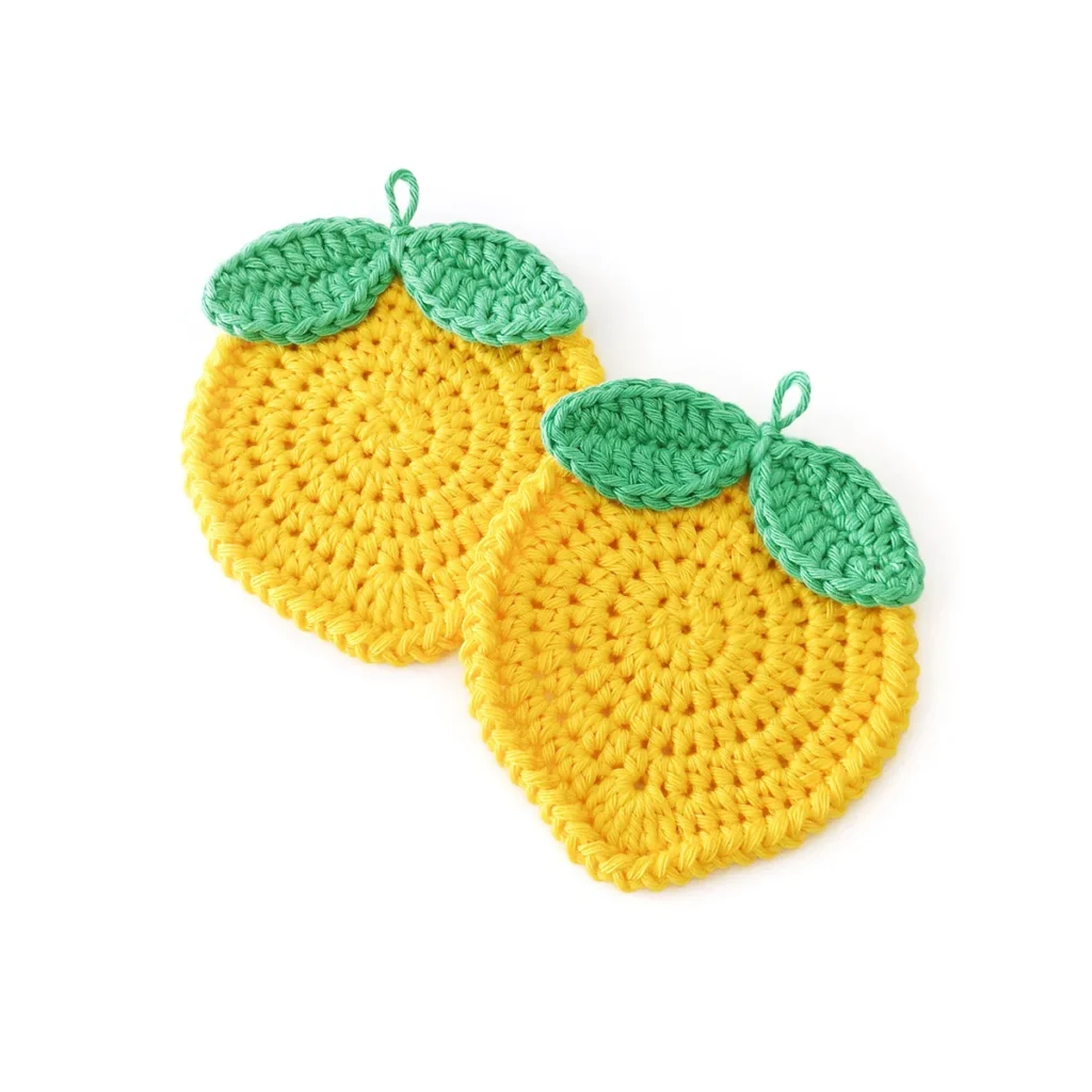 Two crochet lemon coasters with green leaves, lying on a white background, slightly overlapping.