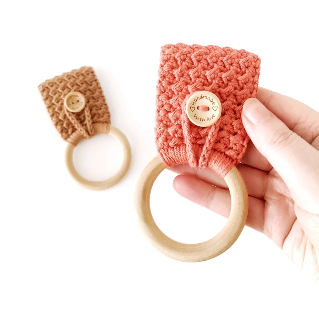 Two crochet towel holders with button loop closures and wooden rings, one brown and one terracotta, being held up against a white background.