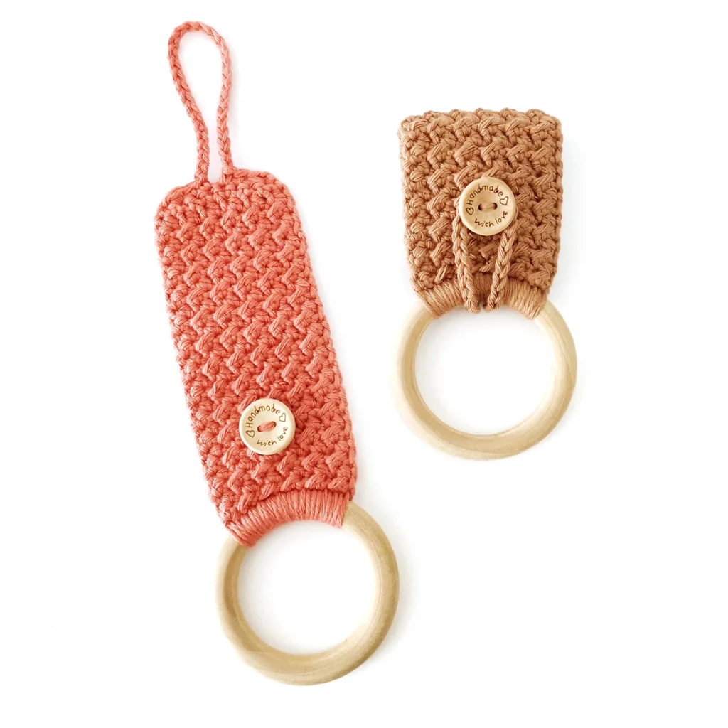 Two crochet towel holders with button loop closures and wooden rings, one brown and one terracotta lying open, on a white background.