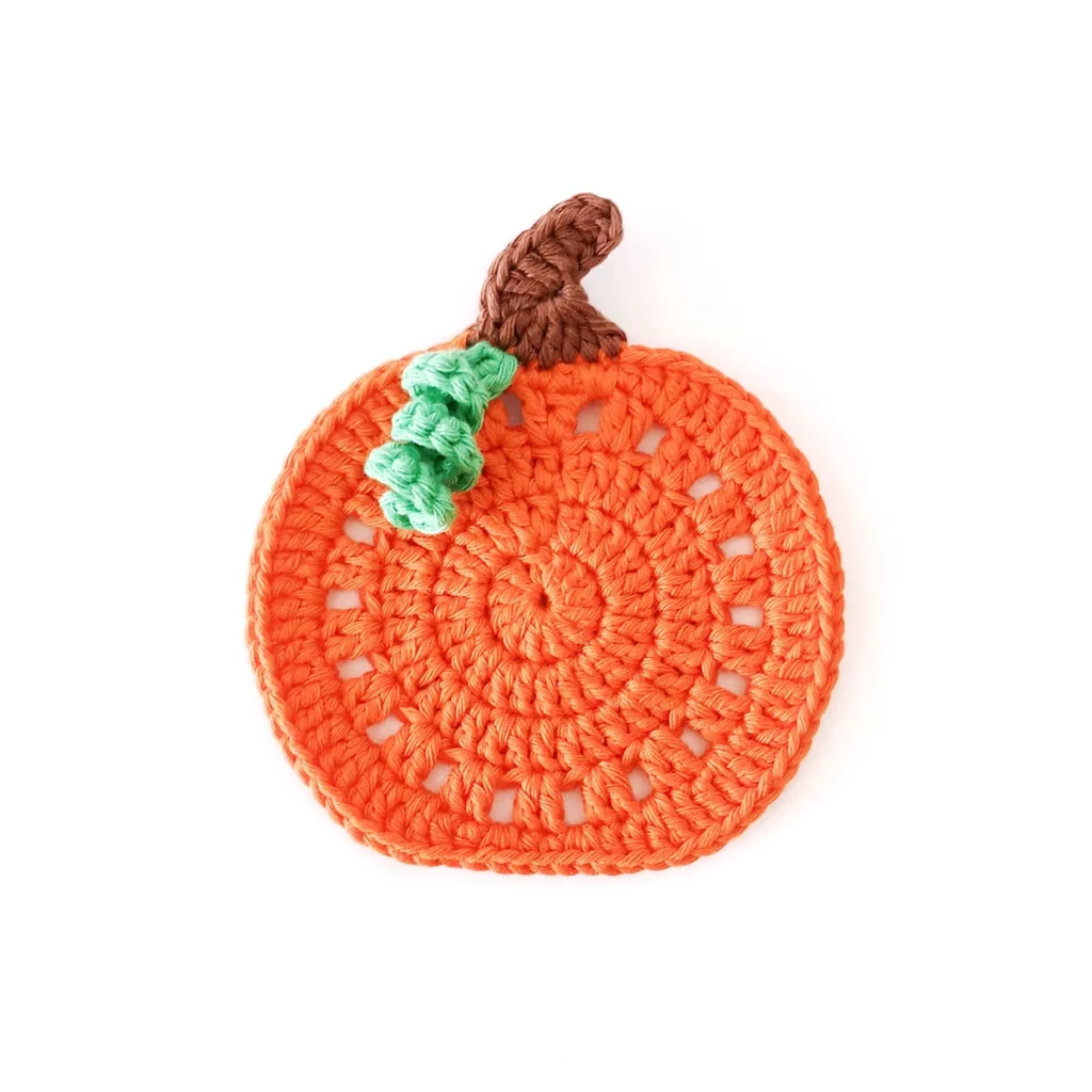 An orange crochet pumpkin coaster with brown stem and small green vine.